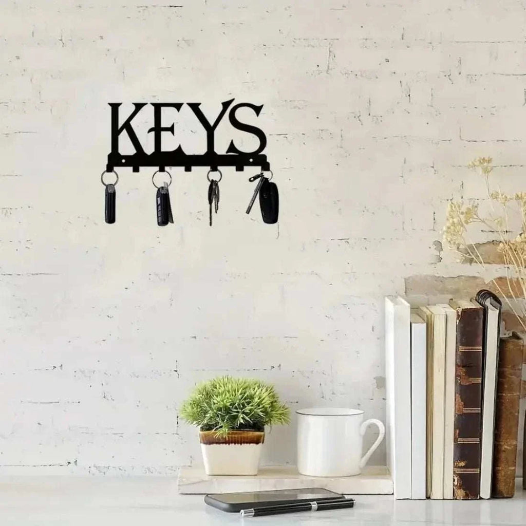 wall mounted black metal key holder with keys hanging on white brick wall above table with books plant and mug