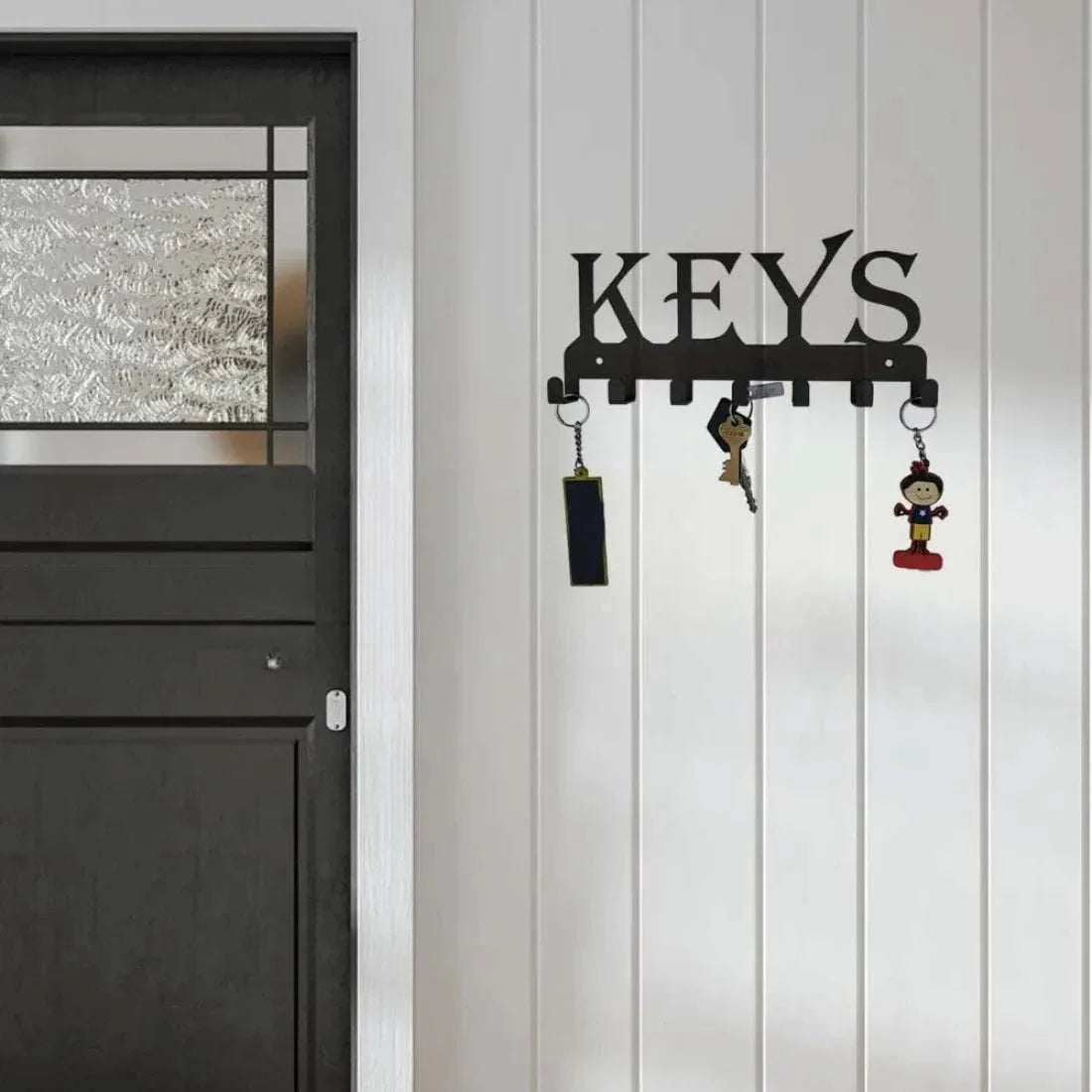 Wall mounted black metal key holder with KEYS sign and hooks for keys hanging on white wall next to black door