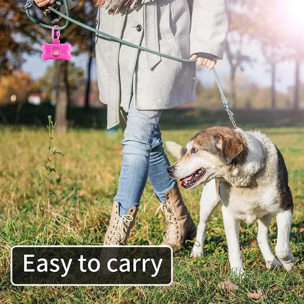 Person walking dog with portable bone-shaped dog poop bag dispenser attached to leash, outdoors