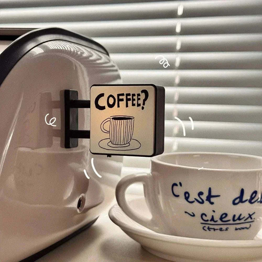 Mini lightbox fridge magnet with coffee cup design attached to white appliance next to a coffee cup and saucer
