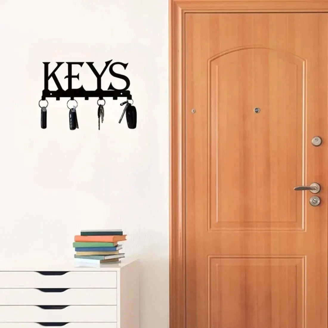 Wall mounted black metal key holder with hooks spelling "KEYS" and hanging keychains near wooden door